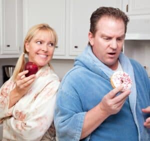 Couple in Kitchen Eating Donut and Coffee or Healthy Fruit.